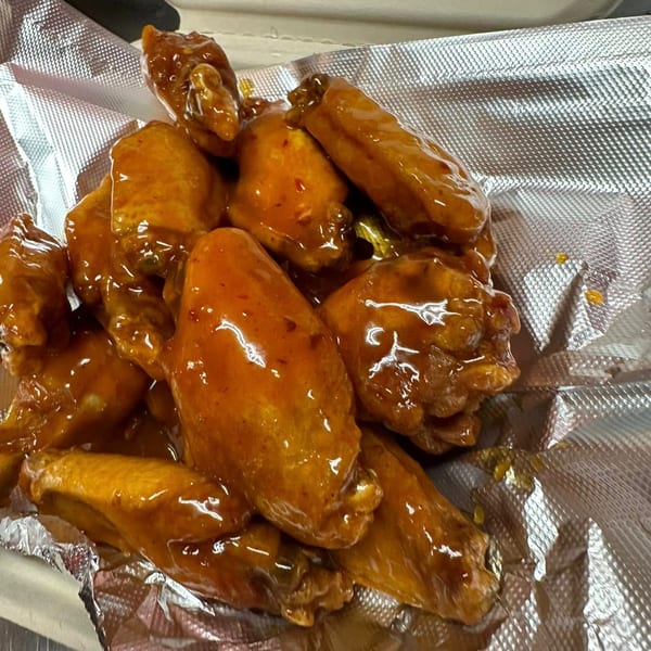 A close-up of Lina's honey garlic wings, glistening with sauce in a foil-lined container.