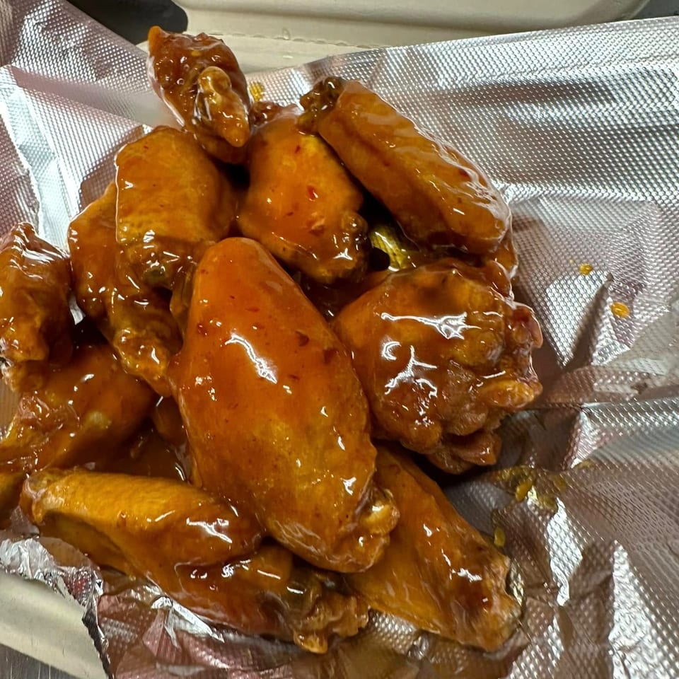 A close-up of Lina's honey garlic wings, glistening with sauce in a foil-lined container.