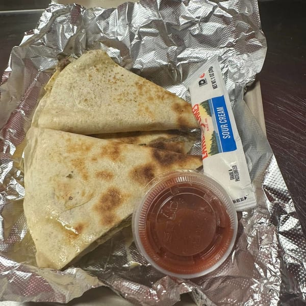 Two quesadilla slices with a side of salsa and a sour cream packet in a foil-lined container.
