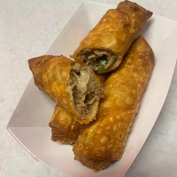 Three crispy egg rolls, one cut open to reveal a savory filling, in a white paper tray.